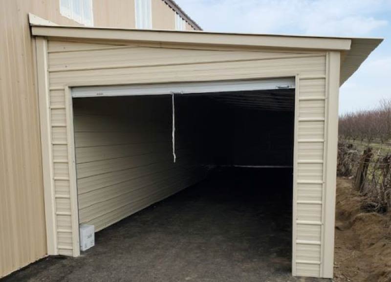 Custom beige single pitch lean-to steel structure attached to a main metal building with a wide open garage door entry.