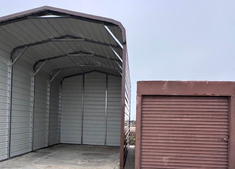 Large beige double-door steel building garage with an open two-car entry and integrated side walk-in door on a gravel driveway.