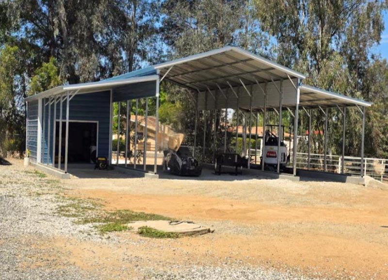 A large commercial-grade blue steel utility building configured with an enclosed workshop bay and a massive open clear-span carport canopy sheltering heavy agricultural tractor equipment.