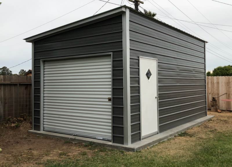 Modern charcoal gray single pitch lean-to metal shed featuring a front rollup door and a white side pedestrian entry door.
