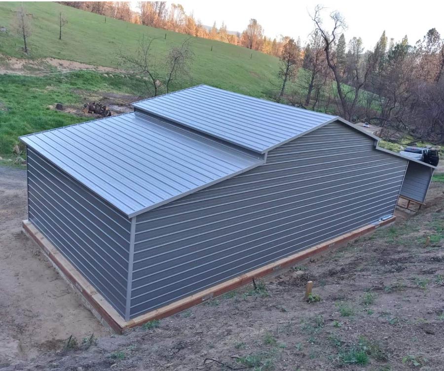 Fully enclosed multi-level gray horizontal steel building garage with a stepped roofline installed on a hillside timber foundation.