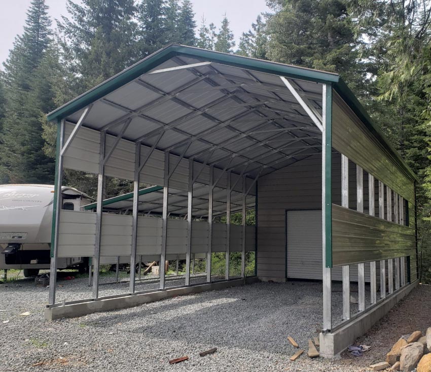 High-clearance green-trimmed steel RV garage building featuring partially open slatted walls, a gravel floor, and a rear rollup door access point.