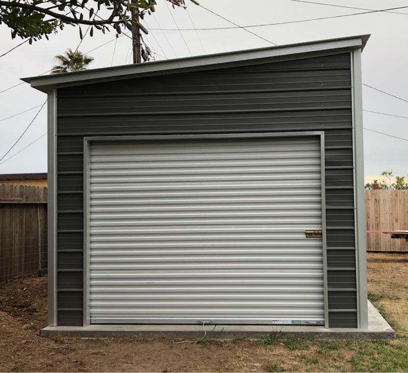 Enclosed dark gray single pitch lean-to steel building garage featuring a secure white rolling shutter door on a concrete foundation pad.