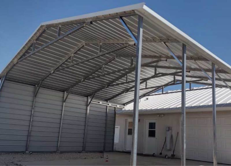 High-clearance open metal carport structure featuring an un-walled side panel and exposed internal steel framing attached next to a residential house.