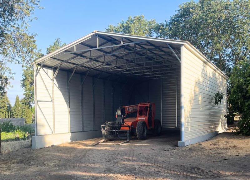 High-clearance steel agricultural equipment storage building with a light beige exterior housing a heavy-duty industrial tractor loader.
