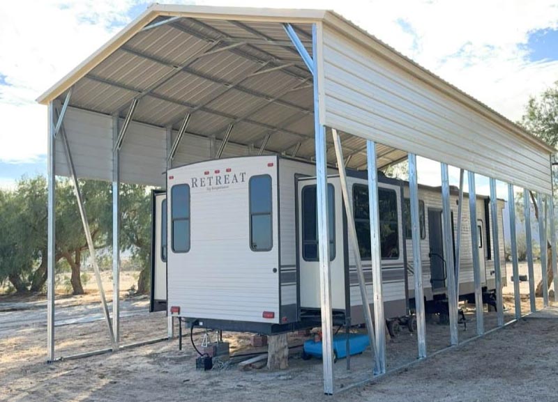 Wide regular-style curved roof metal RV carport installed over an outdoor living patio deck and a parked white travel trailer.