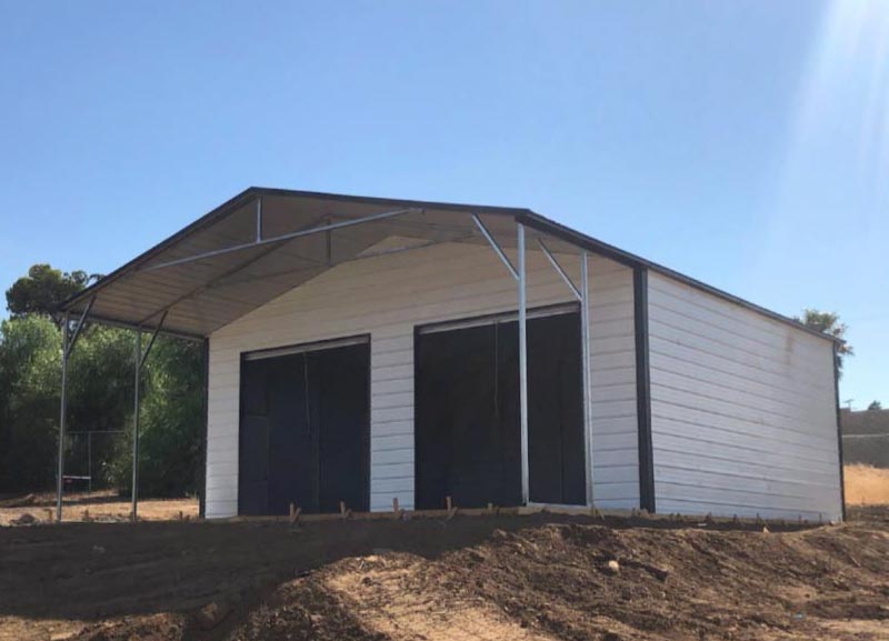A custom white steel utility building featuring a secure dual-bay enclosed garage section paired with an attached open-front metal carport canopy under a durable vertical gabled roofline.